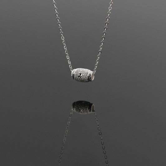 Front 3/4 view of a dainty sparkle textured barrel sterling silver pendant necklace hanging, with a plain reflective gray background.