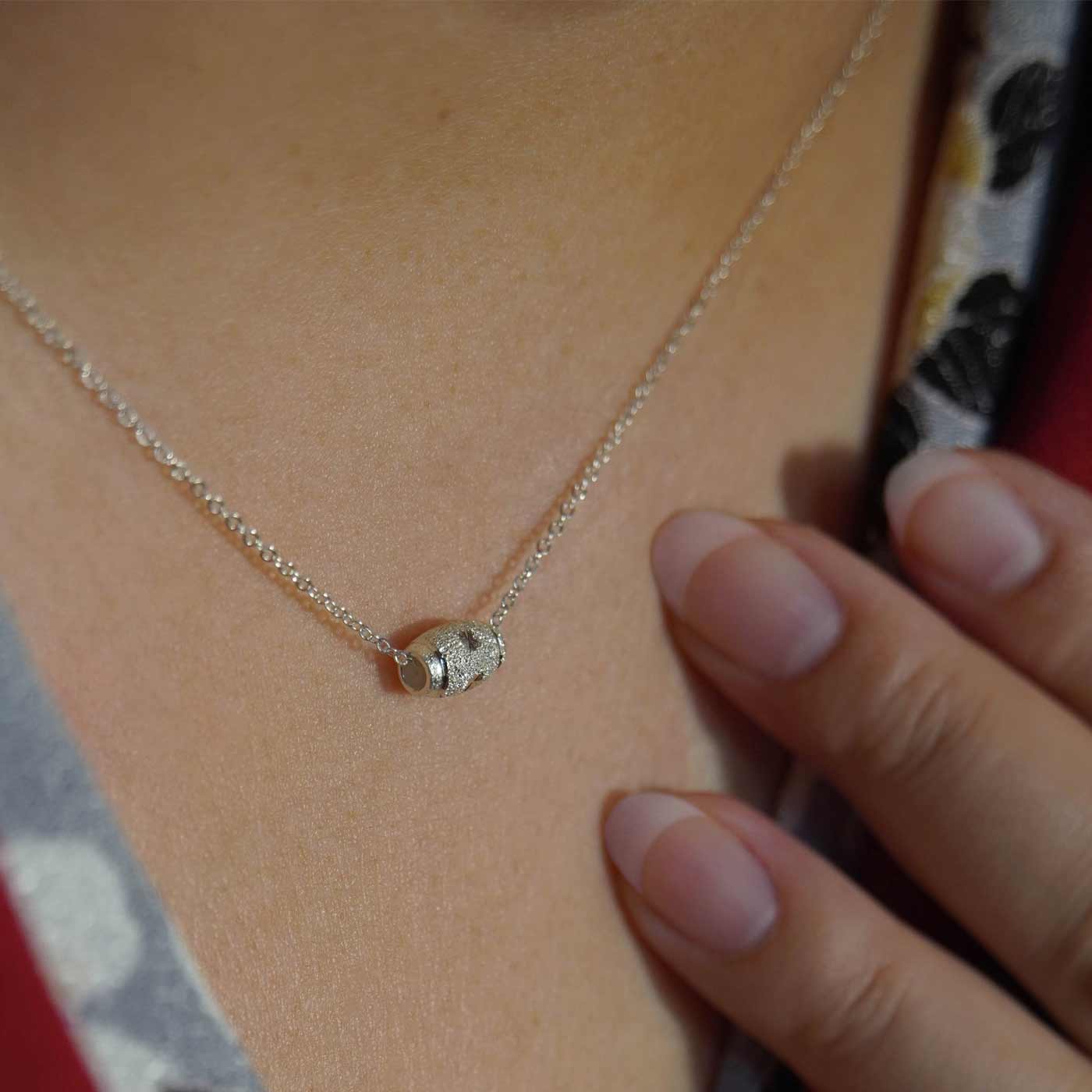Dainty adjustable chain sterling silver textured sparkly barrel pendant necklace worn by a person wearing a beautiful Japanese Kimono in red with black, gray and white floral pattern with nails and hand in view.