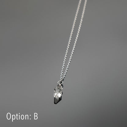 Bottom front view of a dainty, high quality AAA clear raw Herkimer Diamond Quartz wire wrapped sterling silver pendant necklace, laying flat on a plain reflective gray background.