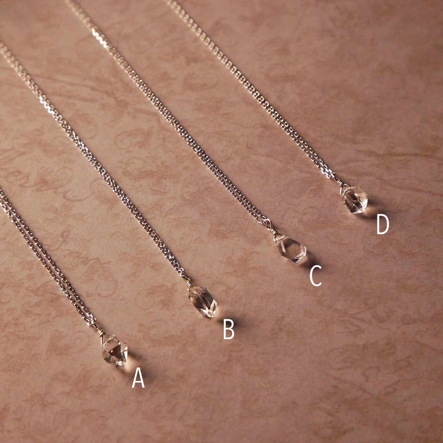 Top angle view of 4 high quality AAA dainty Herkimer Diamond Quartz wire wrapped pendant chain necklaces in sterling silver. They are stylized laying flat on vintage patterned pinkish beige paper underneath.