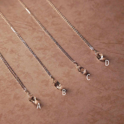 Top angle view of 4 high quality AAA dainty Herkimer Diamond Quartz wire wrapped pendant chain necklaces in sterling silver. They are stylized laying flat on vintage patterned pinkish beige paper underneath.