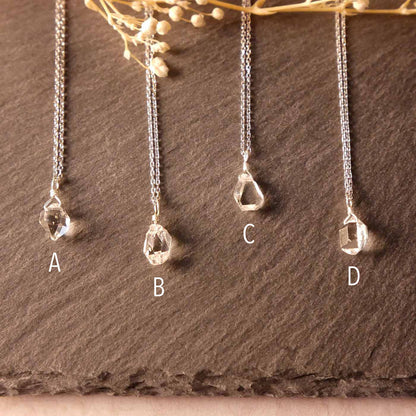 Top front view of 4 high quality AAA dainty Herkimer Diamond Quartz wire wrapped pendant chain necklaces in sterling silver. They are stylized laying flat on a dark gray slate surface with dried baby's breath flowers on top in the foreground.