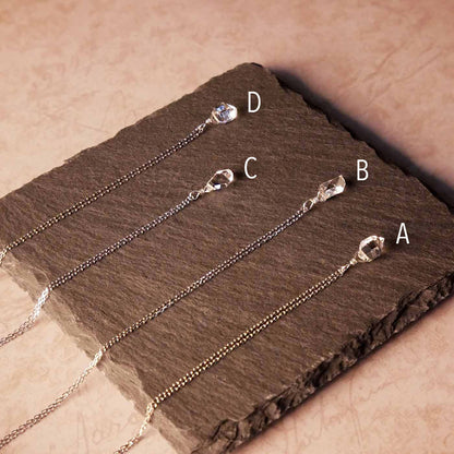 Top back angle view of 4 high quality AAA dainty Herkimer Diamond Quartz wire wrapped pendant chain necklaces in sterling silver. They are stylized laying flat on a dark gray slate surface with vintage pink beige paper underneath.