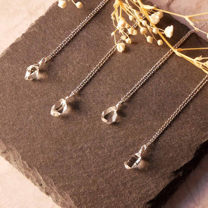 Top angle view of 4 high quality AAA dainty Herkimer Diamond Quartz wire wrapped pendant chain necklaces in sterling silver. They are stylized laying flat on a dark gray slate surface with dried baby's breath flowers in the foreground.