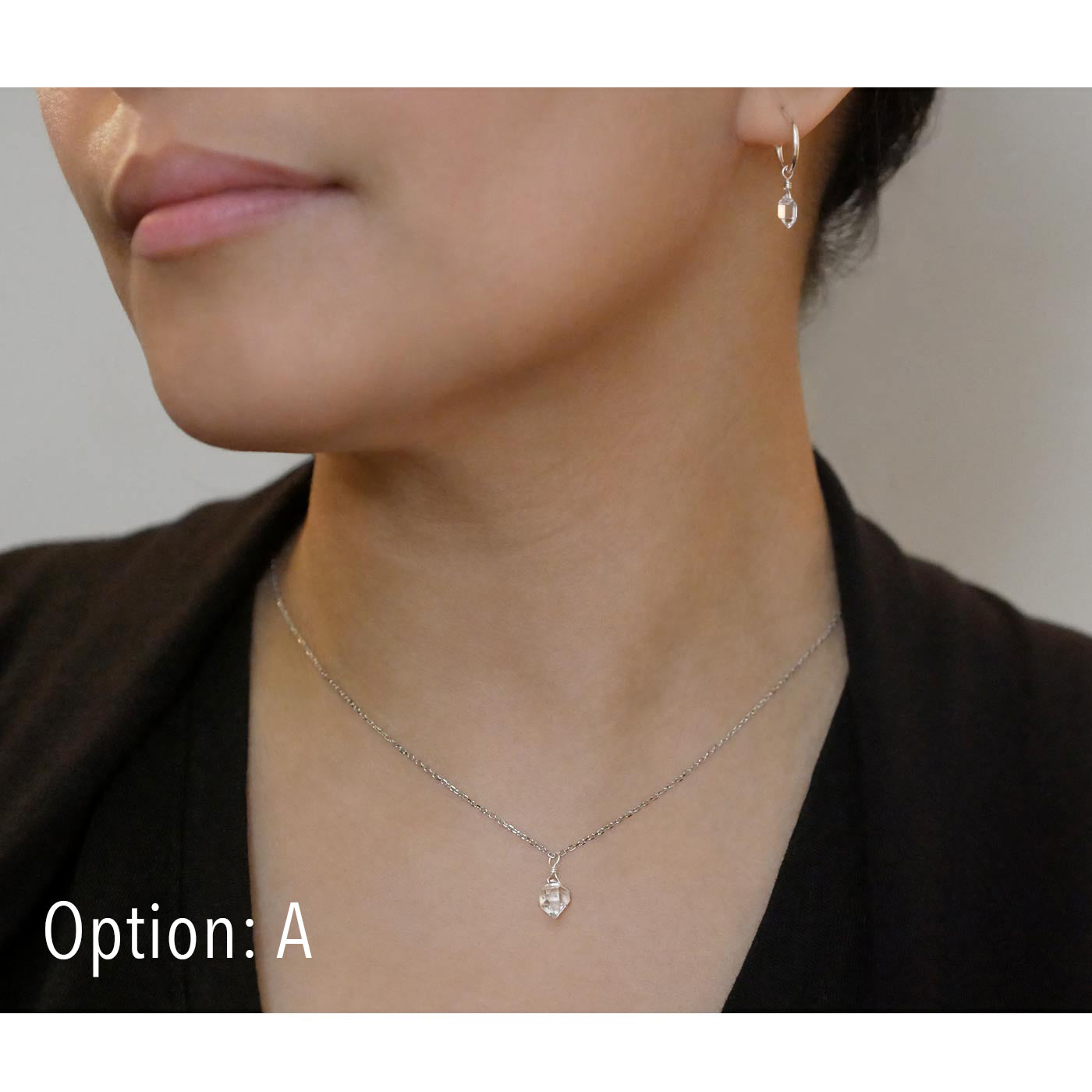 Close-up of a person wearing a dainty high quality AAA Herkimer Diamond Quartz wire wrapped pendant chain necklace and matching Herkimer earring hoops in sterling silver. The person has on a black top and sweater.