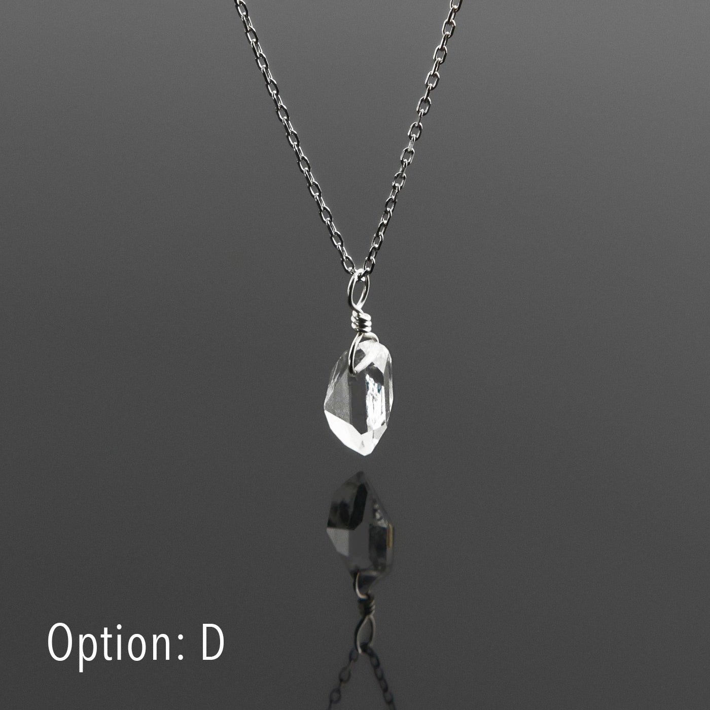 Side view of a dainty, high quality AAA clear raw Herkimer Diamond Quartz wire wrapped sterling silver pendant necklace hanging, with a plain reflective gray background.
