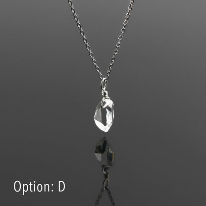 Side view of a dainty, high quality AAA clear raw Herkimer Diamond Quartz wire wrapped sterling silver pendant necklace hanging, with a plain reflective gray background.