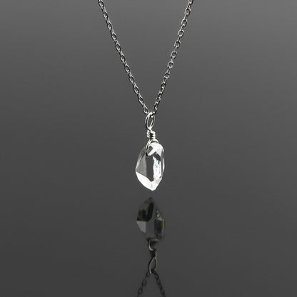 Side view of a dainty, high quality AAA clear raw Herkimer Diamond Quartz wire wrapped sterling silver pendant necklace hanging, with a plain reflective gray background.