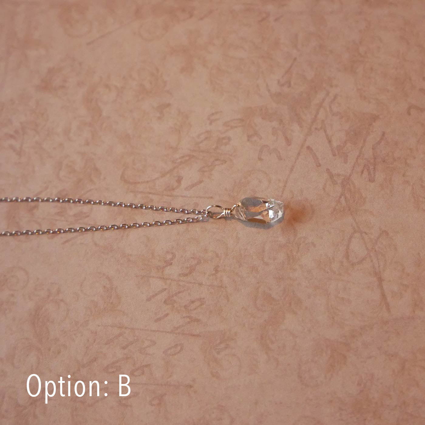 Top side view of a high quality AAA dainty Herkimer Diamond Quartz wire wrapped pendant chain necklace in sterling silver. It is stylized laying flat over vintage cursive writing numbers patterned pinkish beige paper underneath.
