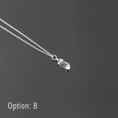 3/4 view of a dainty, high quality AAA clear raw Herkimer Diamond Quartz wire wrapped sterling silver pendant necklace, laying flat on a plain reflective gray background.