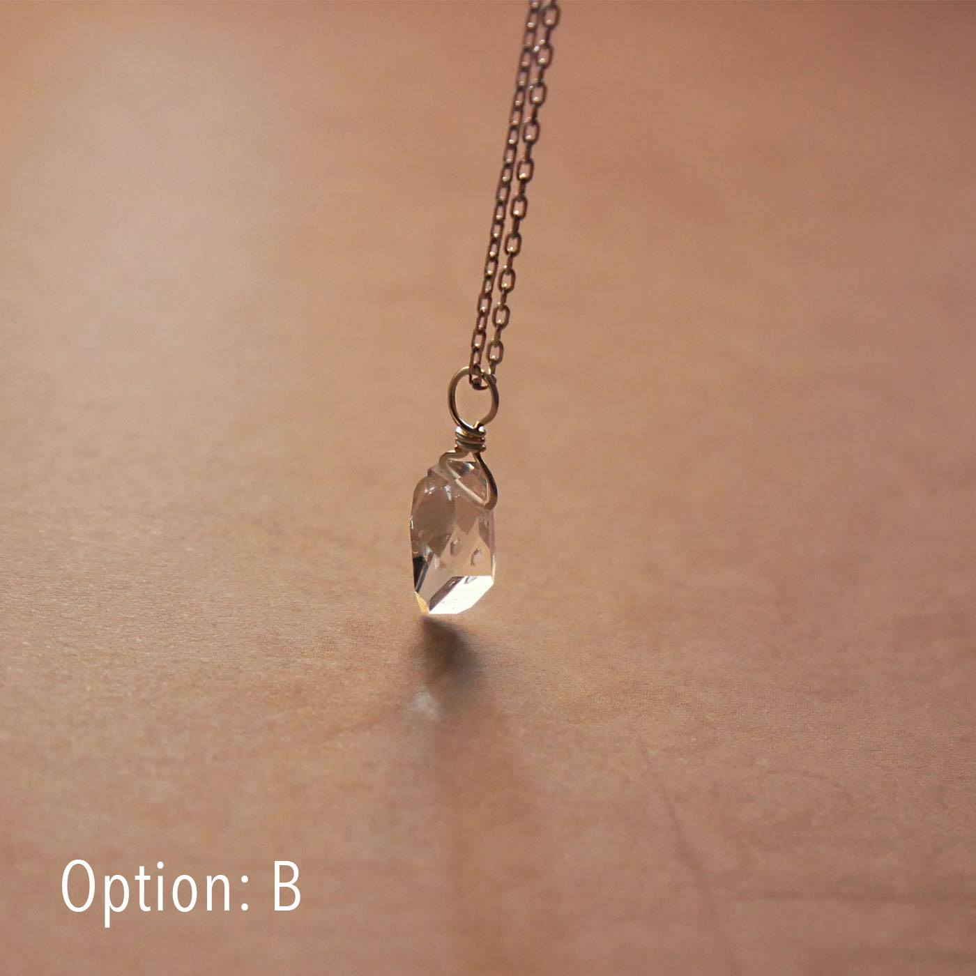 High quality AAA dainty Herkimer Diamond Quartz wire wrapped pendant chain necklace in sterling silver. It is stylized hanging from above over vintage patterned pinkish beige paper underneath.