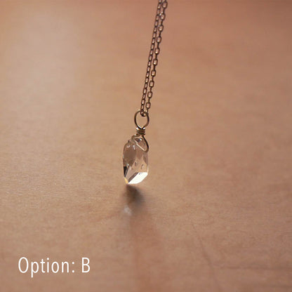 High quality AAA dainty Herkimer Diamond Quartz wire wrapped pendant chain necklace in sterling silver. It is stylized hanging from above over vintage patterned pinkish beige paper underneath.