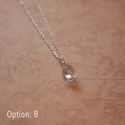 High quality AAA dainty Herkimer Diamond Quartz wire wrapped pendant chain necklace in sterling silver. It is stylized laying flat over vintage patterned pinkish beige paper underneath.