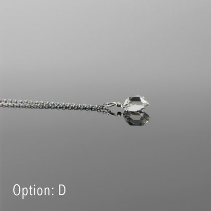 Side view of a dainty, high quality AAA clear raw Herkimer Diamond Quartz wire wrapped sterling silver pendant necklace, laying flat on a plain reflective gray background.