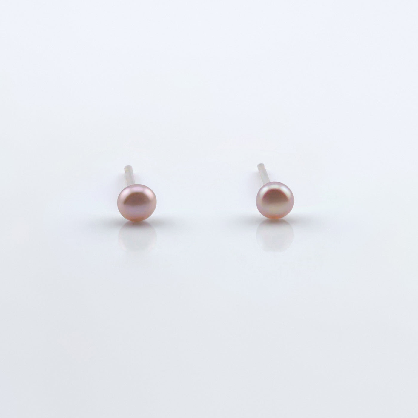 Front view of a pair of dainty natural pink pearl stud earrings on plain white background.