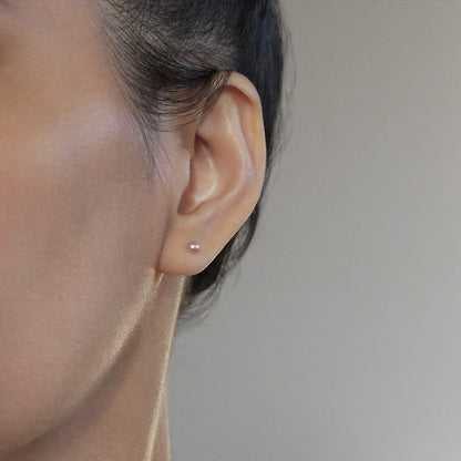 Close-up of dainty minimalist natural pink pearl sterling silver earrings worn on a person with dark hair.