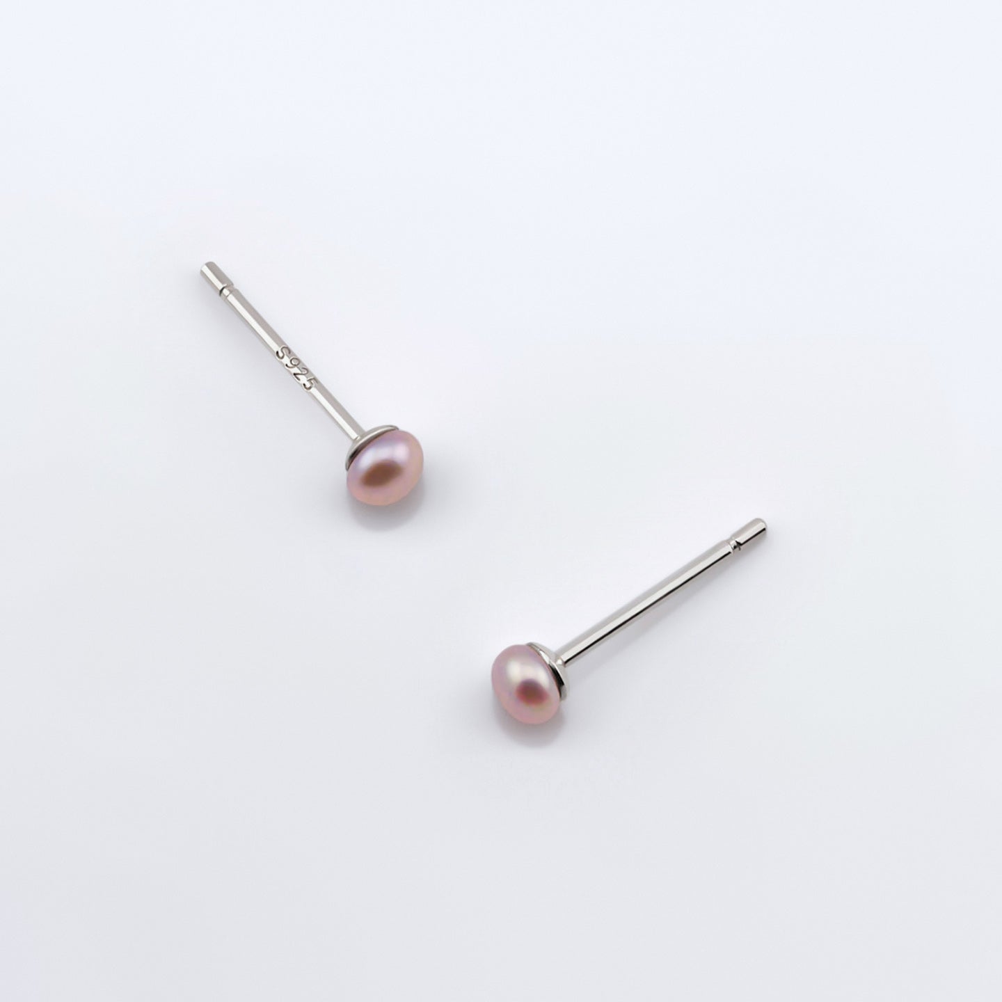 Top view of a pair of minimalist dainty natural pink pearl stud earrings laying flat on plain white background.