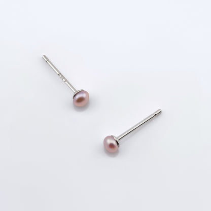 Top view of a pair of minimalist dainty natural pink pearl stud earrings laying flat on plain white background.
