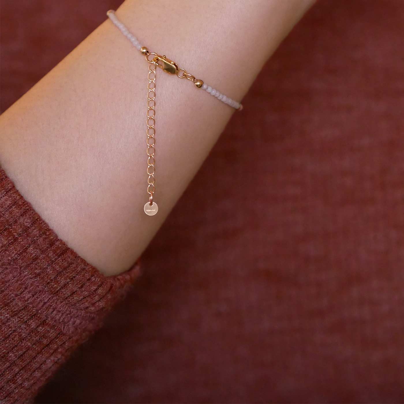 Close up of a person wearing a brown long sleeve shirt, wearing on their wrist a dainty beaded bracelet with smooth amazonite beads, rice pearls and 14K gold filled accent beads, clasp, and extender chain hanging.