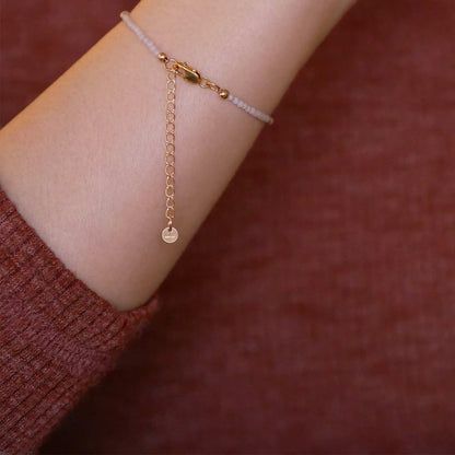 Close up of a person wearing a brown long sleeve shirt, wearing on their wrist a dainty beaded bracelet with smooth amazonite beads, rice pearls and 14K gold filled accent beads, clasp, and extender chain hanging.