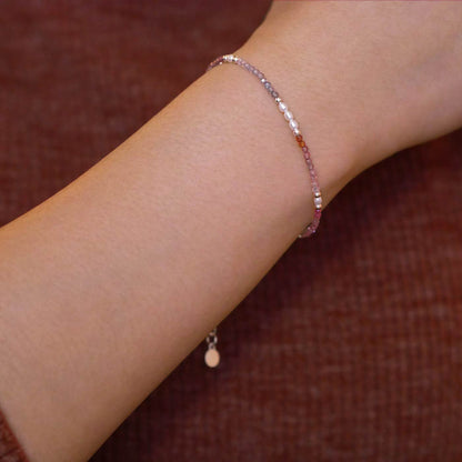 Close-up of a wrist wearing dainty  faceted ombre colorful spinel and accent rice pearls high quality AAA beaded bracelet, with sterling silver accent beads. The background is a person wearing a brown long sleeve sweater.