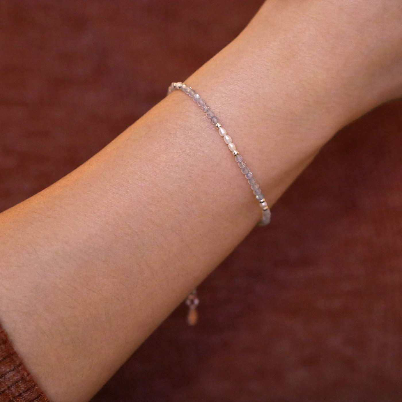 Close up of a person wearing a brown long sleeve shirt, wearing on their wrist a dainty beaded bracelet with AAA quality faceted natural labradorites, rice pearls and sterling silver accent beads.