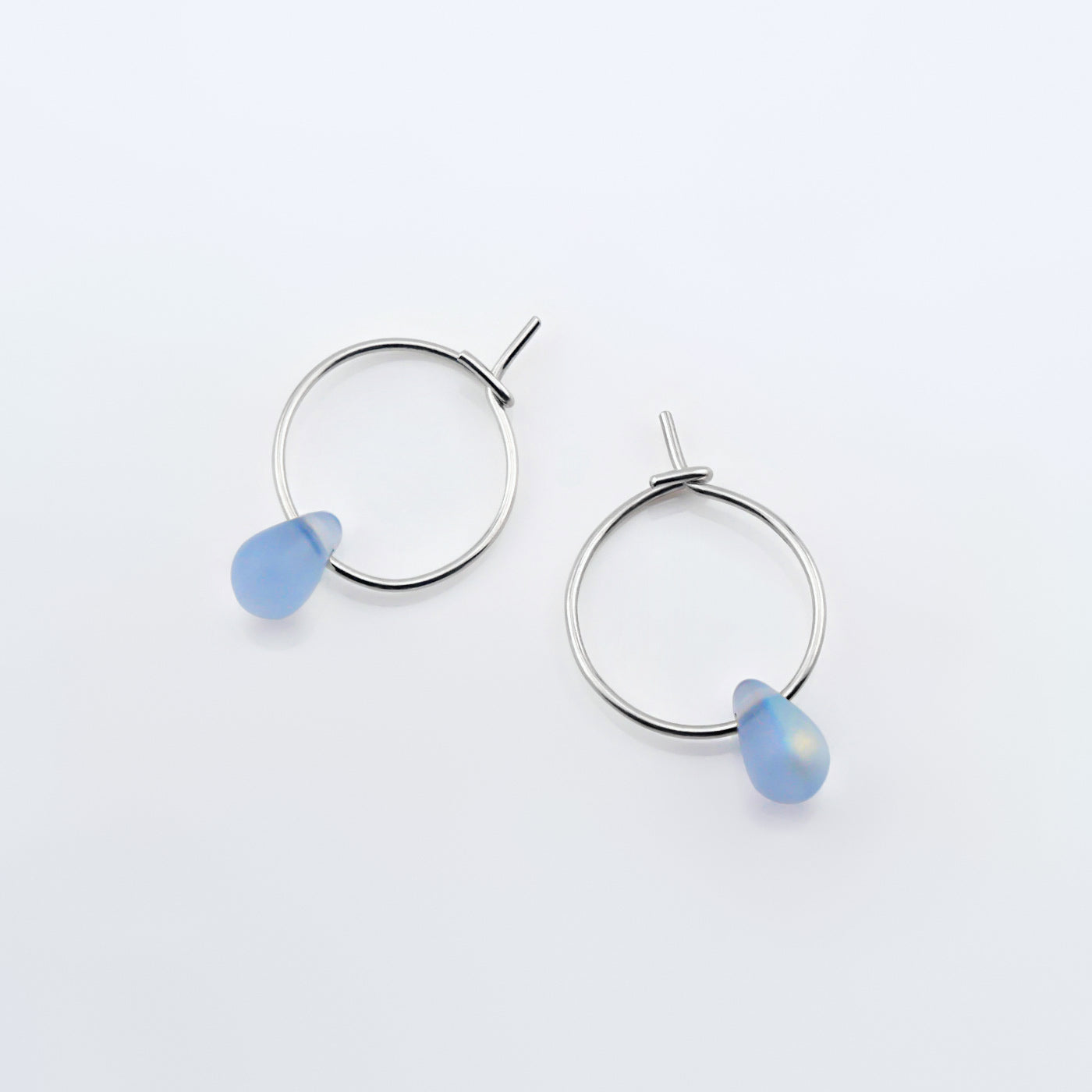 Top view of a pair of sterling silver Czech glass crystal AB aurora borealis colored drop wire hoop earrings, laying flat on a plain white background.