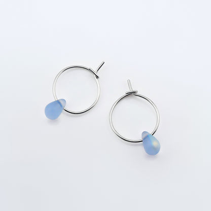 Top view of a pair of sterling silver Czech glass crystal AB aurora borealis colored drop wire hoop earrings, laying flat on a plain white background.