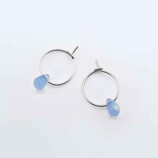 Top view of a pair of sterling silver Czech glass crystal AB aurora borealis colored drop wire hoop earrings, laying flat on a plain white background.