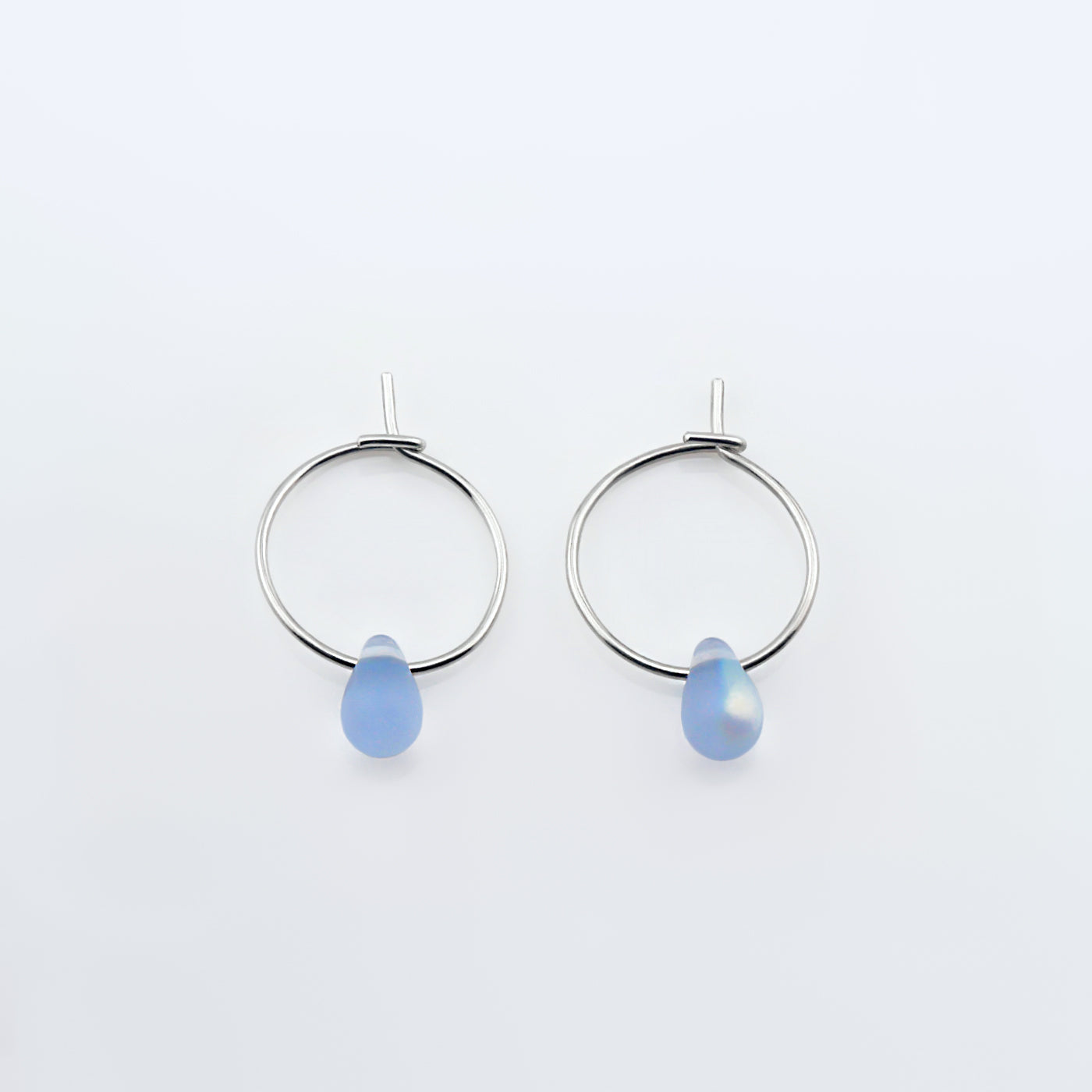Top view of a pair of sterling silver Czech glass crystal AB aurora borealis colored drop wire hoop earrings, laying flat on a plain white background.