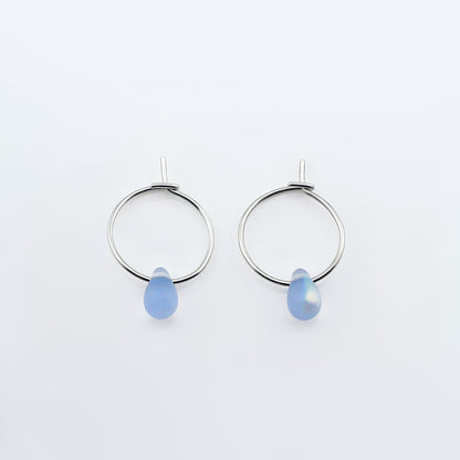 Top view of a pair of sterling silver Czech glass crystal AB aurora borealis colored drop wire hoop earrings, laying flat on a plain white background.