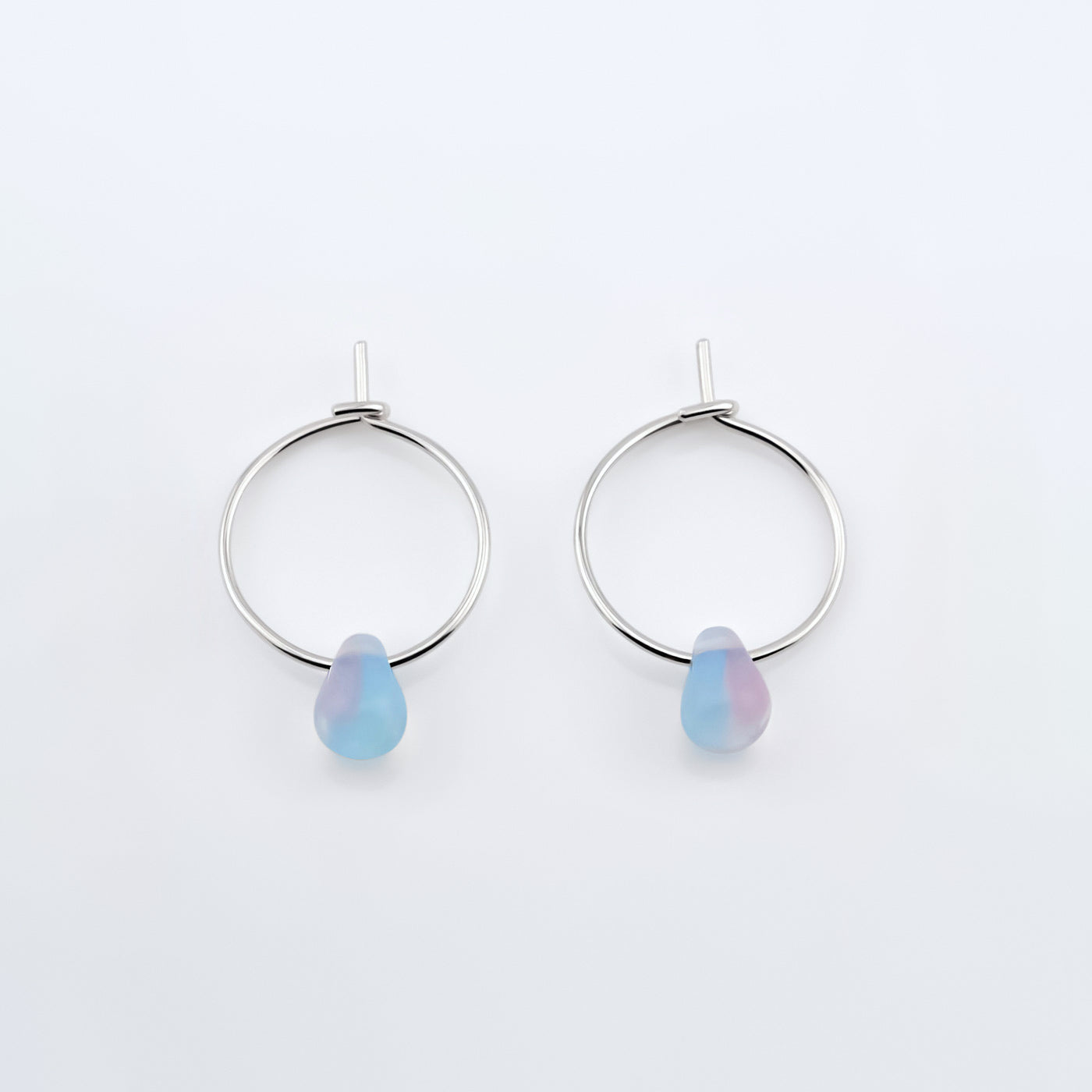 Top view of a pair of sterling silver Czech glass crystal milky blue pink colored drop wire hoop earrings, laying flat on a plain white background.
