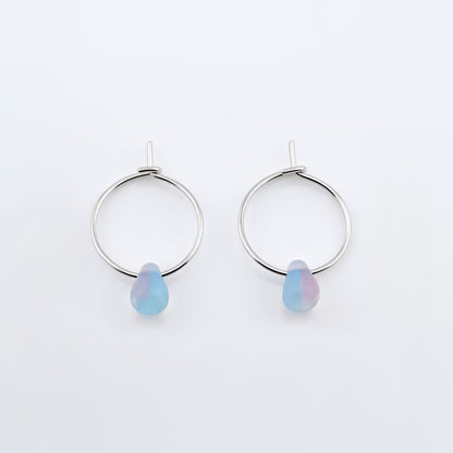 Top view of a pair of sterling silver Czech glass crystal milky blue pink colored drop wire hoop earrings, laying flat on a plain white background.