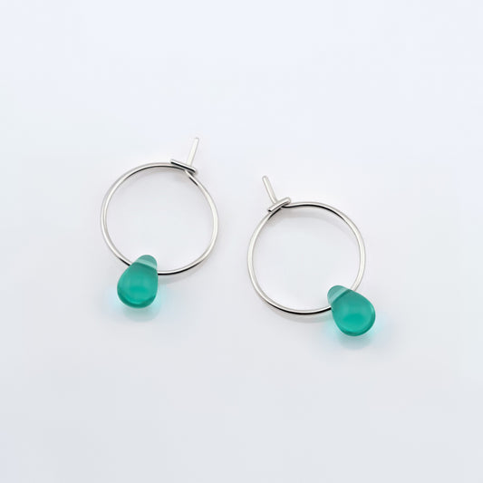 Top view of a pair of sterling silver Czech glass crystal teal colored drop wire hoop earrings, laying flat on a plain white background.