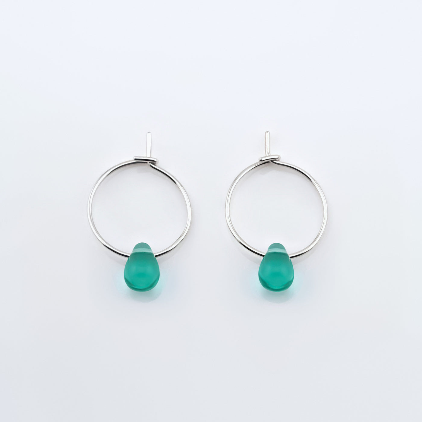 Top view of a pair of sterling silver Czech glass crystal teal colored drop wire hoop earrings, laying flat on a plain white background.