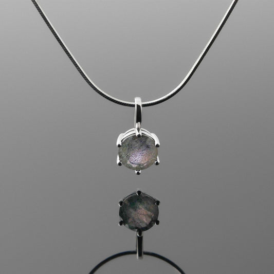Front view of a dainty, round high quality Labradorite prong set pendant sterling silver necklace hanging, with a plain reflective gray background.