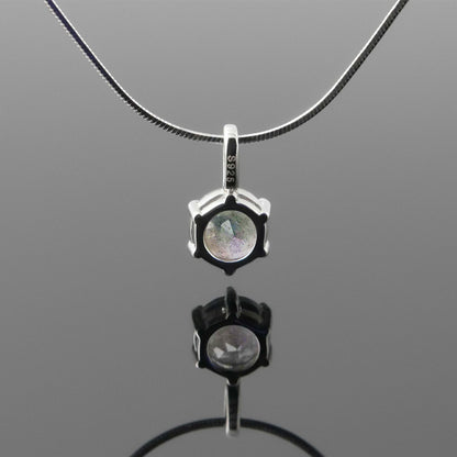 Back view of a dainty, round high quality Labradorite prong set pendant sterling silver necklace hanging, with a plain reflective gray background.