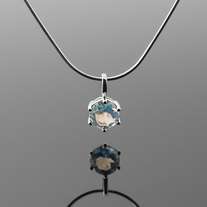 Front view of a dainty, round high quality eye clean faceted AAA Rainbow Blue Moonstone prong set pendant sterling silver necklace hanging, with a plain reflective gray background.