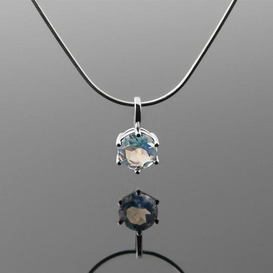 Front view of a dainty, round high quality eye clean faceted AAA Rainbow Blue Moonstone prong set pendant sterling silver necklace hanging, with a plain reflective gray background.