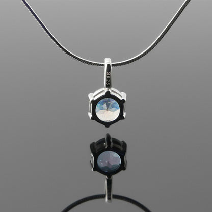 Back view of a dainty, round high quality eye clean faceted AAA Rainbow Blue Moonstone prong set pendant sterling silver necklace hanging, with a plain reflective gray background.