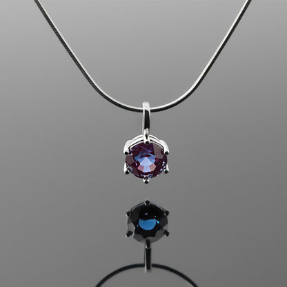 Front view of a dainty, round high quality eye clean faceted AAA Chrysoberyl lab grown genuine authentic Alexandrite prong set pendant sterling silver necklace hanging, with a plain reflective gray background.