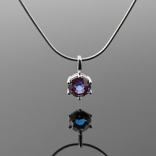 Front view of a dainty, round high quality eye clean faceted AAA Chrysoberyl lab grown genuine authentic Alexandrite prong set pendant sterling silver necklace hanging, with a plain reflective gray background.