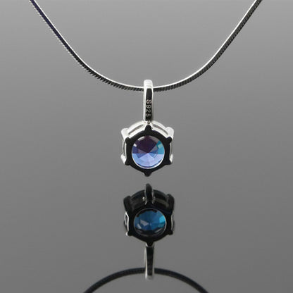 Back view of a dainty, round high quality eye clean faceted AAA Chrysoberyl lab grown genuine authentic Alexandrite prong set pendant sterling silver necklace hanging, with a plain reflective gray background.